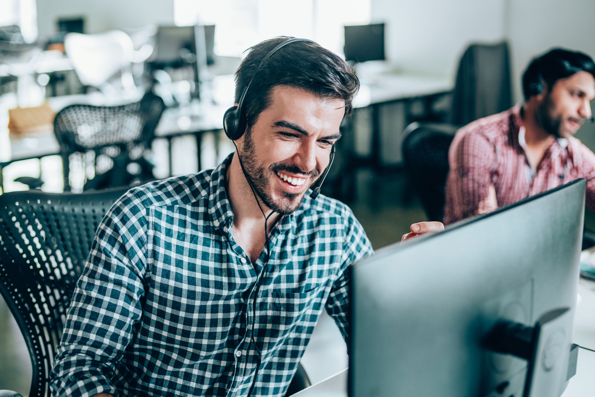 Smiling handsome young businessman working in call center. Shot of a cheerful young man working in a call center with his team. Confident male operator is working with colleagues. Call center operators sitting in a row at desks.