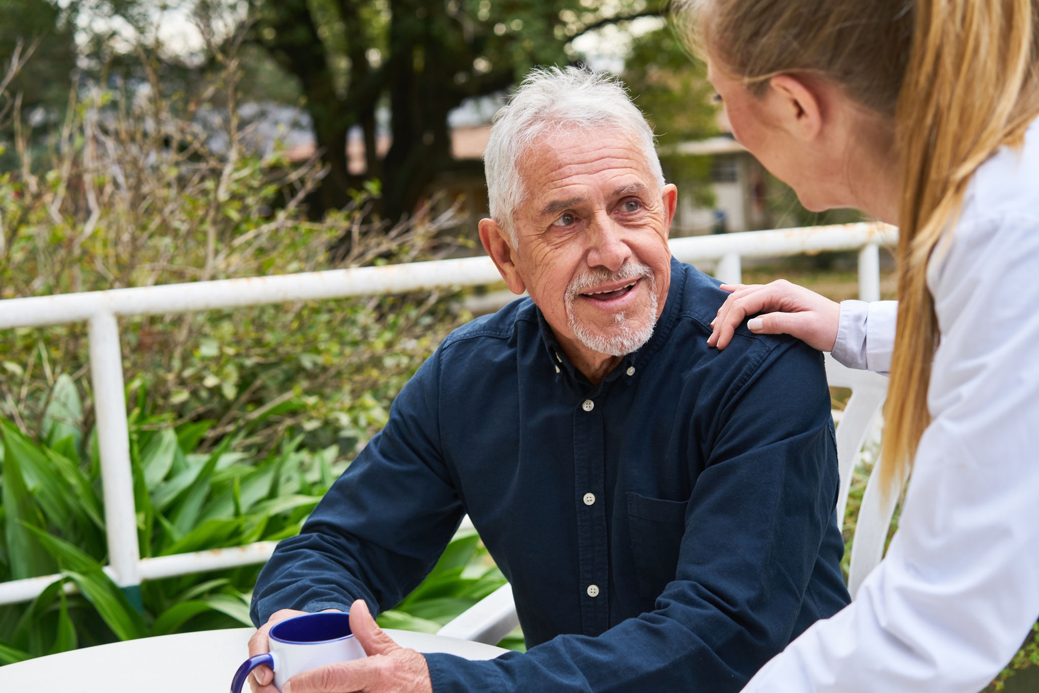 Female doctor consoling smiling elderly man sitting in garden of nursing home