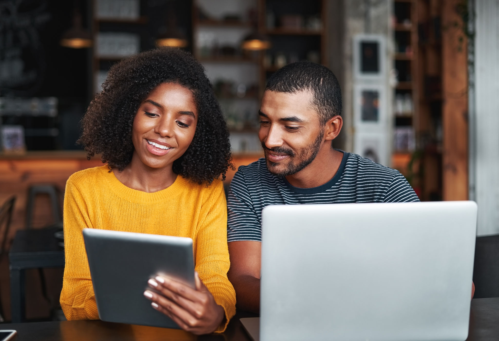 Portrait of an african young woman showing something to her boyfriend on digital tablet in cafe