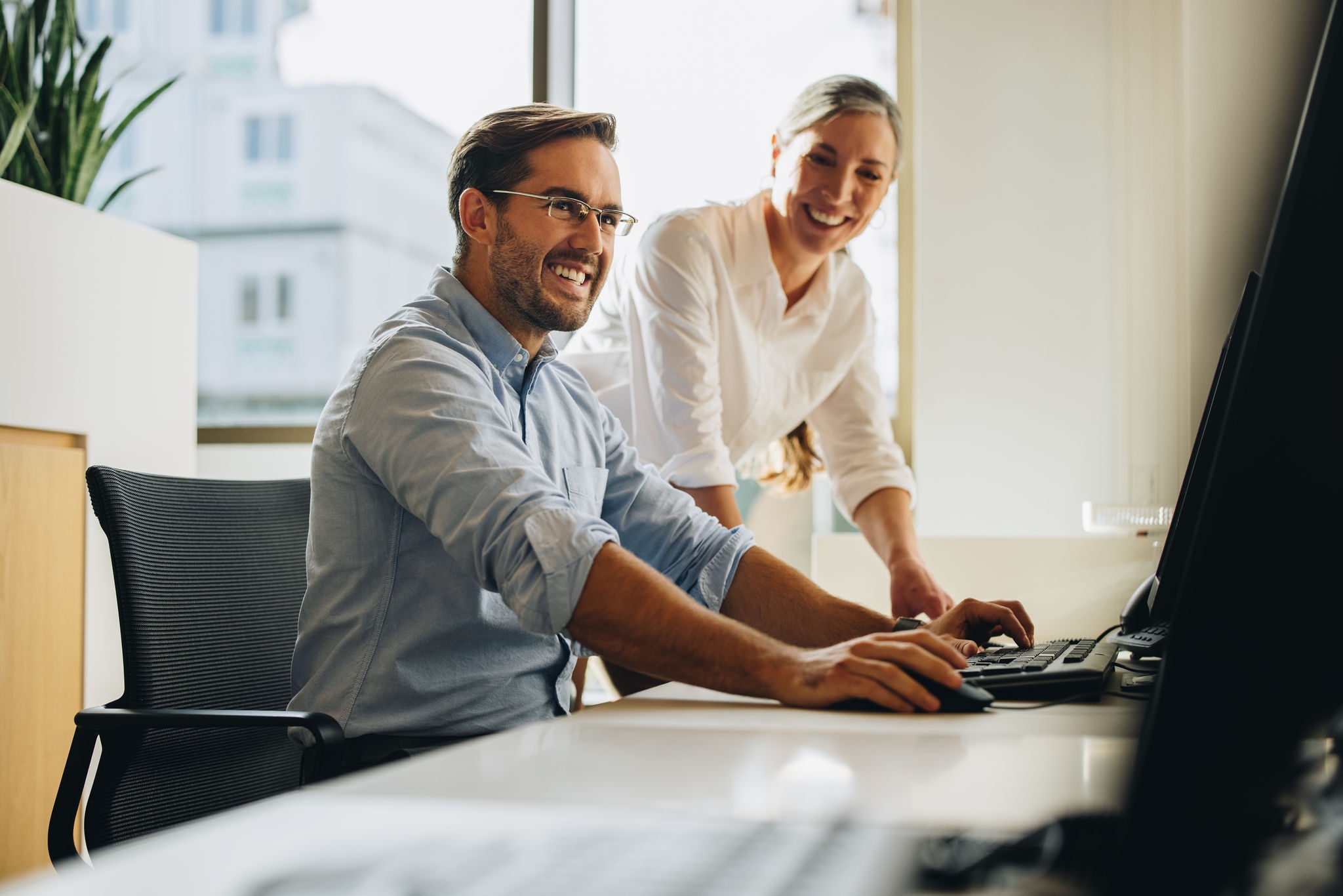 Business partners working together on computer. Colleagues smiling and discussing project on computer.