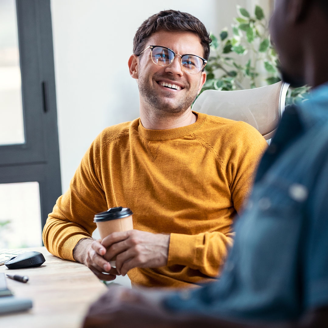 Man in yellow jumper, holding a coffee and smiling