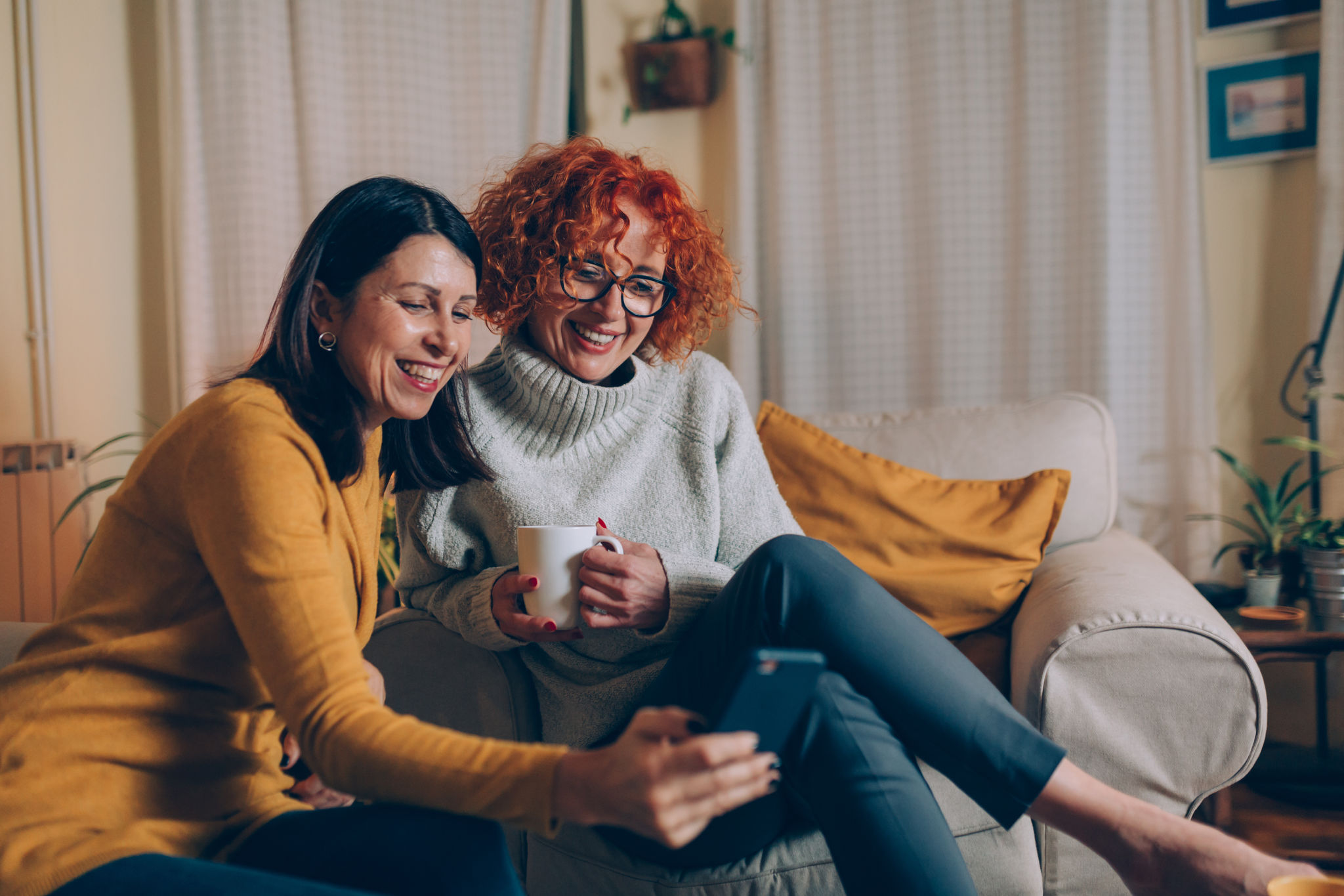 middle aged female friends having fun at home, using mobile phone