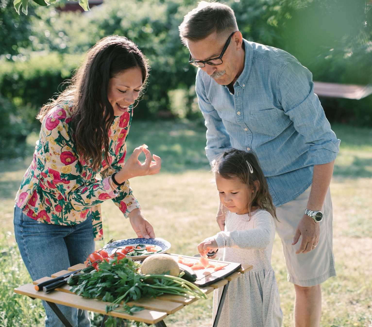 Girl cutting food with mother and grandfather in their backyard