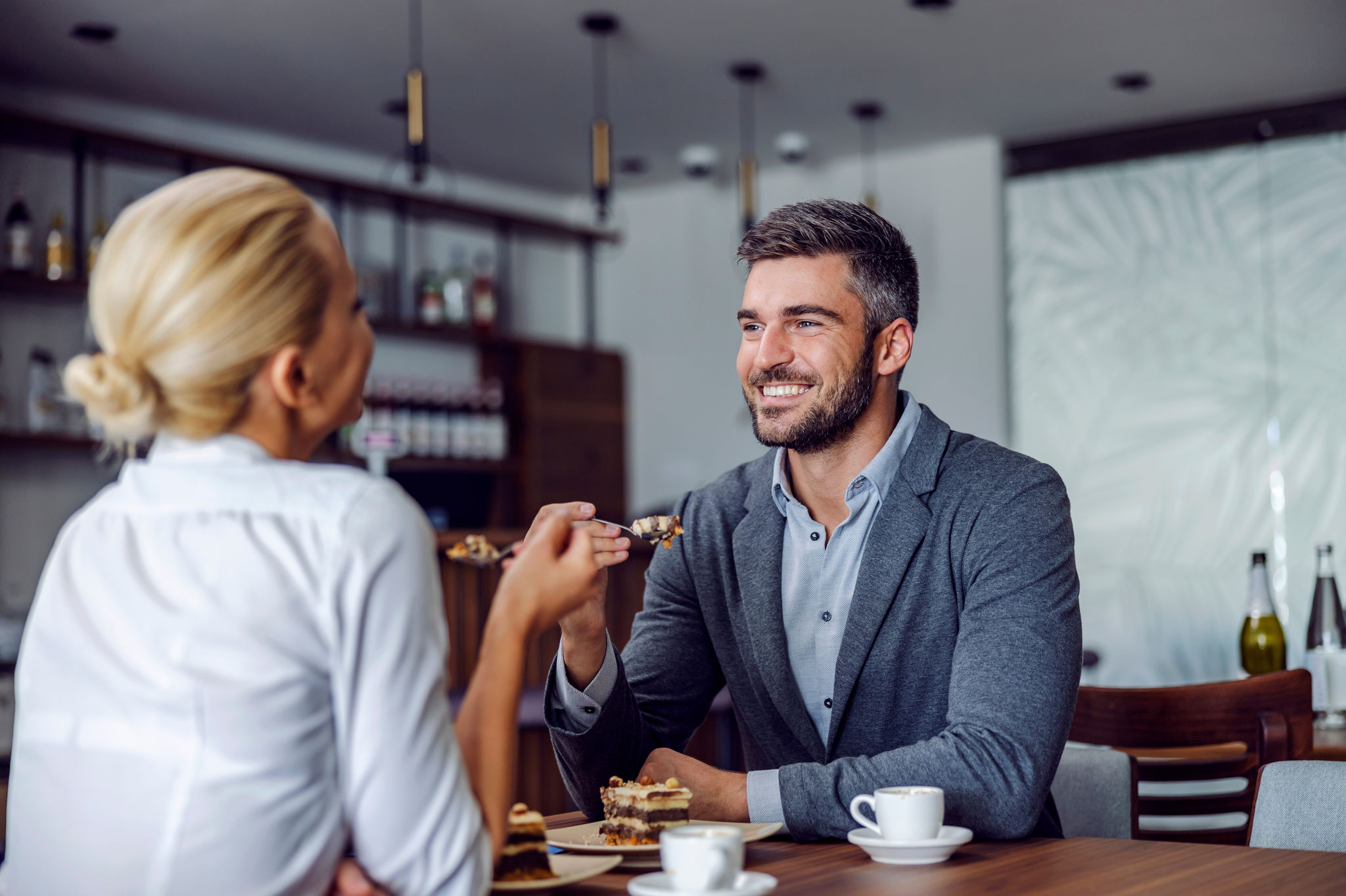 A happy, elegant couple is sitting in the restaurant and having a cake for dessert. Sweet love. Couple eating cake at the coffee shop.