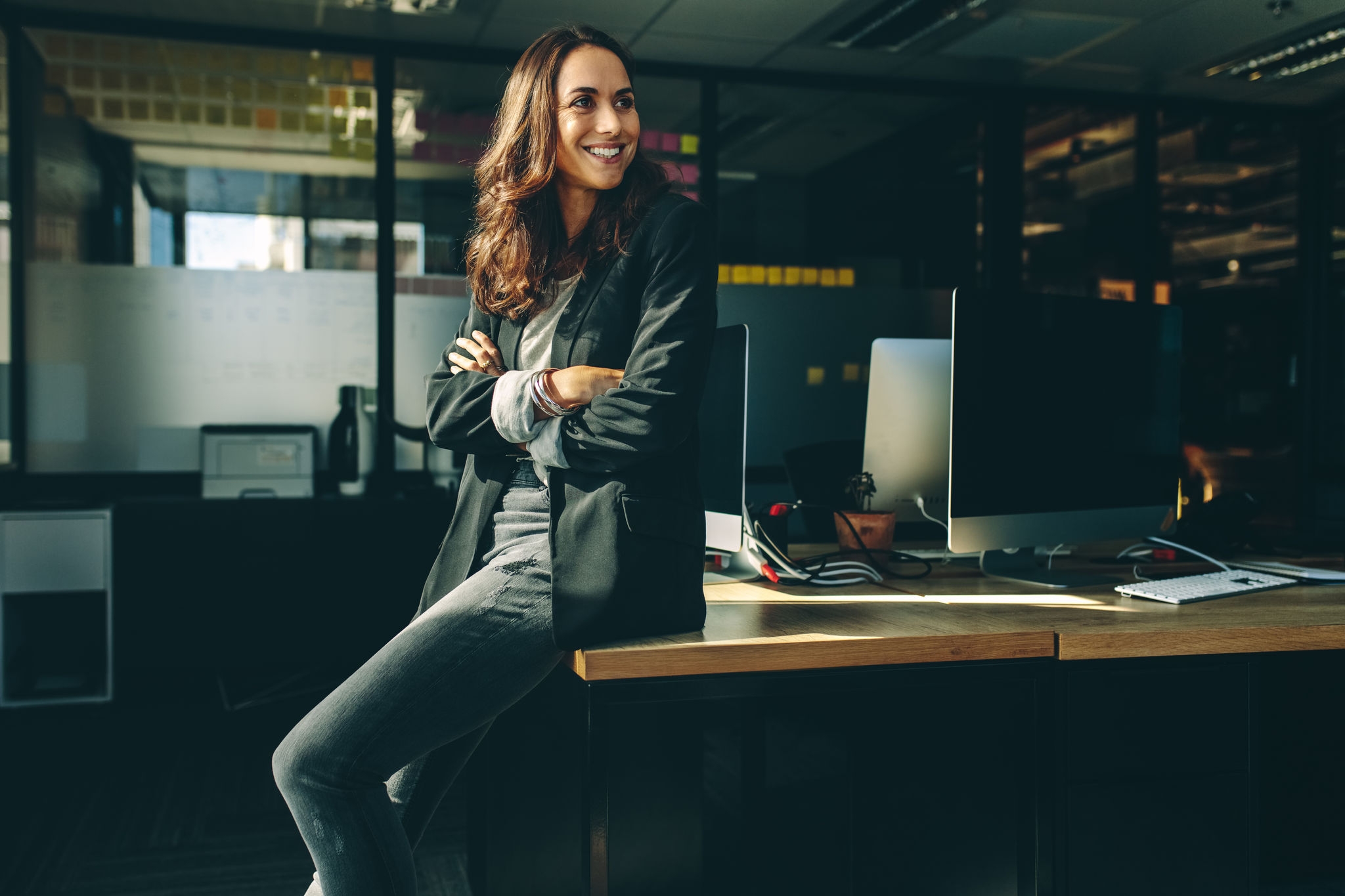 Smiling businesswoman sitting on her desk. Female business professionals sitting in her office looking away and smiling.