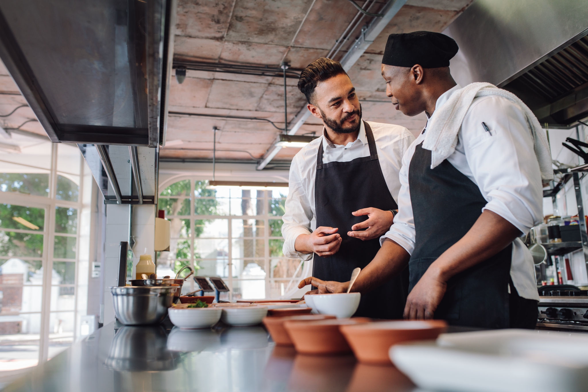 Two male cooks preparing food on restaurant kitchen. Chefs talking while cooking food in commercial kitchen.