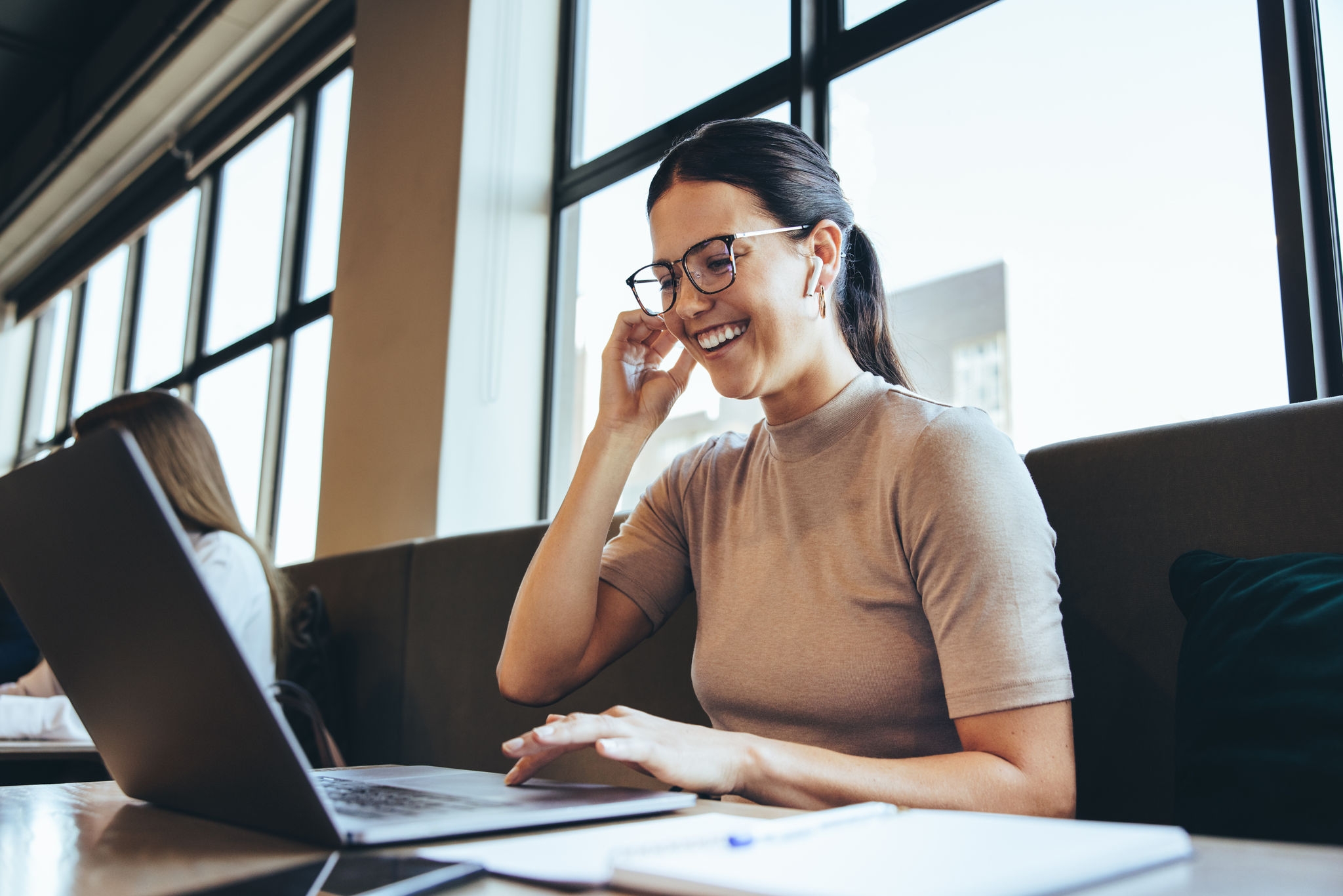 Happy businesswoman taking a video call in a co-working space. Cheerful female entrepreneur smiling during a virtual meeting. Young businesswoman working in a modern workspace.