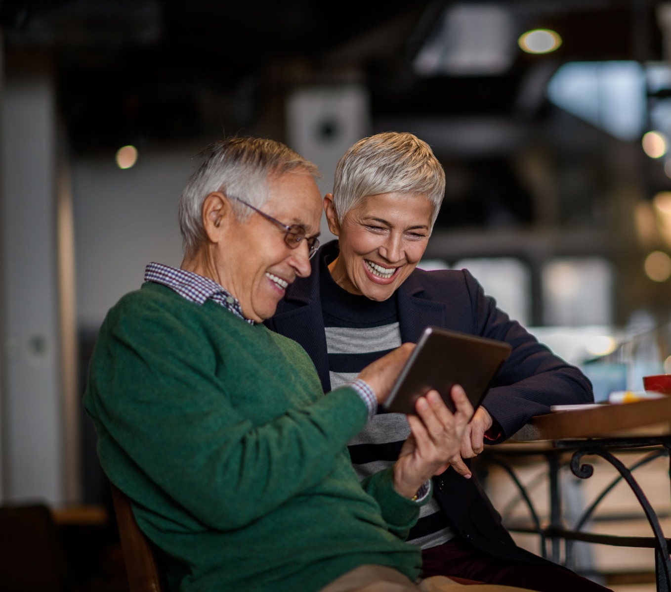 Senior couple having coffee in cafeteria while working on digital tablet.