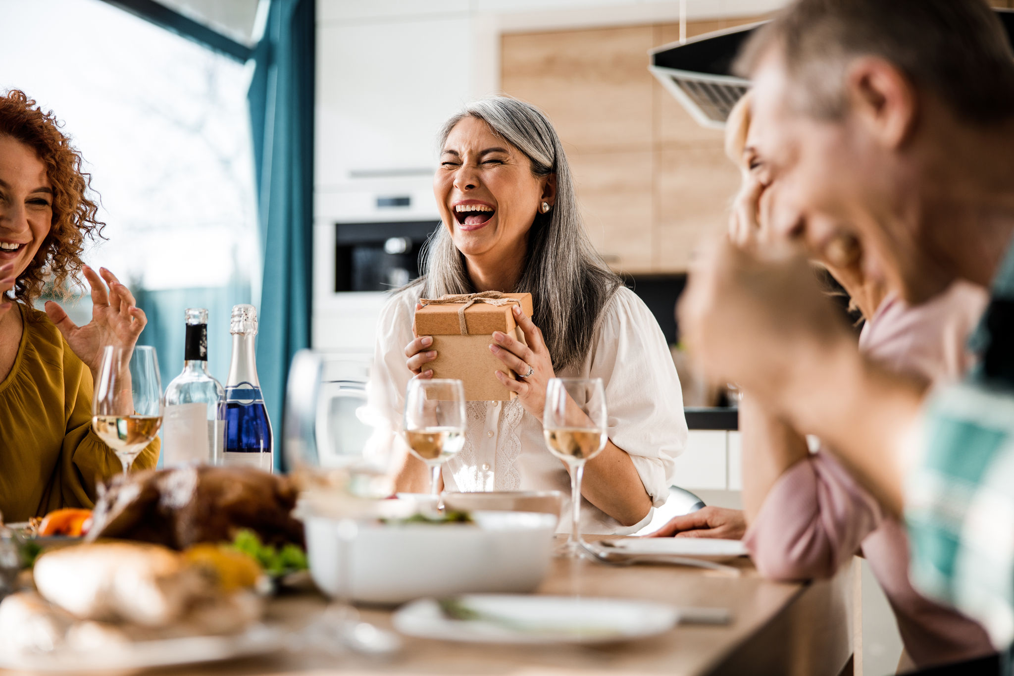 Happy prettty Asian lady holding gift box while laughing at home with her guests