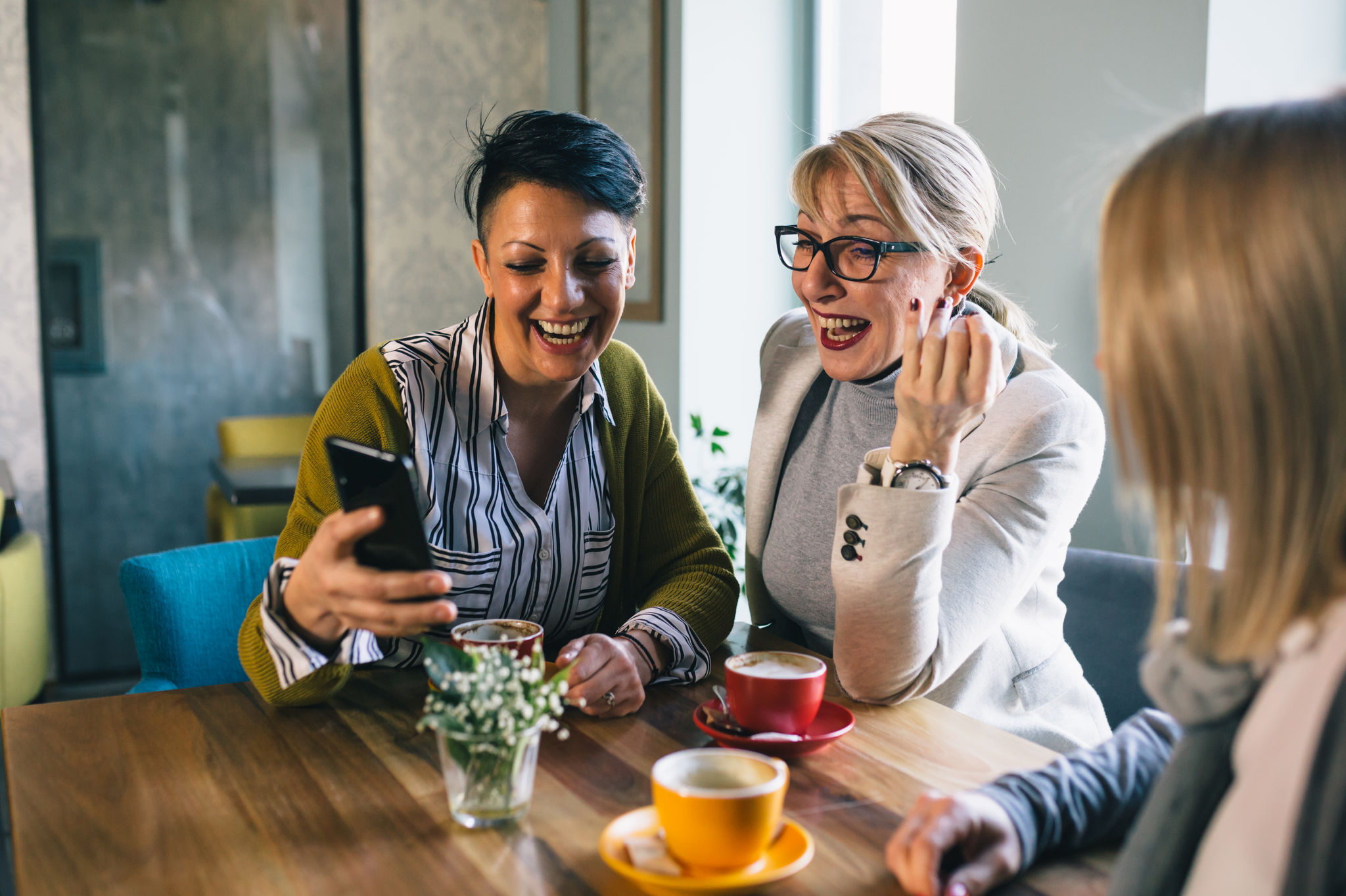 mid aged woman friends talking and drinking coffee in cafe, using mobile phone